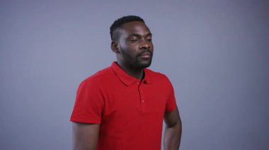 Parlak kırmızı tişörtlü, düşünceli Afro-Amerikan bir adam gri arka planda kameraya bakıyor. Erkek güzeli. Erkek portresi, yakın görünüm