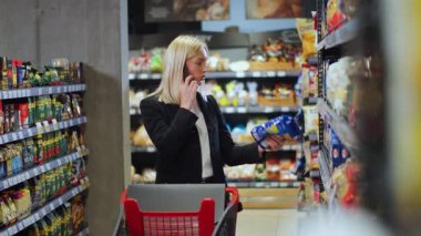 New York - 19 Mayıs 2018: Kocasıyla akıllı telefonda konuşan resmi kadın iş kadını süpermarkette gıda ürünleri seçiyor. Sohbet. İş adamları. Market..