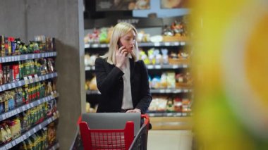 Klasik takım elbiseli resmi iş kadını süpermarketten alışveriş yaparken akıllı telefondan arkadaşını arıyor. Yiyecek alışverişi. Sohbet. Market..