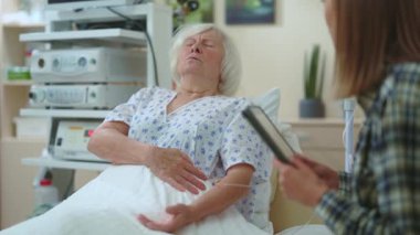 Yaşlı hasta kadın hasta kızıyla hastanede konuşuyor. Ani acı çekiyor. Çok kötü hissediyor. Hapların kavanozunu açmaya çalışan genç bir kadın. Sağlık, hastalık konsepti.