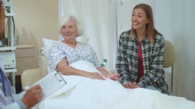 Genç kadın ve yaşlı hastası doktor teşhisi dinliyor. Tıbbi raporlar, özel Clinci Hastanesi 'nde kalmakla ilgili sinir bozucu bir şekilde yoğunlaşıyor..