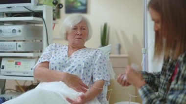 Aşk umudu konsepti: Mutlu Kız, hastanede yatan hasta kadının elini tutuyor, umutla bakıyor, ailesinden destek alırken mutlu bir şekilde gülümsüyor.