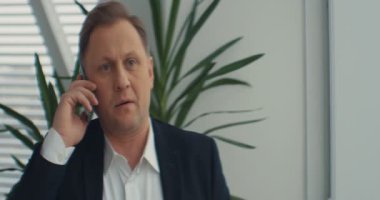İş adamı ofiste telefonla konuşur. Endişeli hissediyorum. Üzücü ve tatminsiz. RED Epic Camera 'da Çekim.