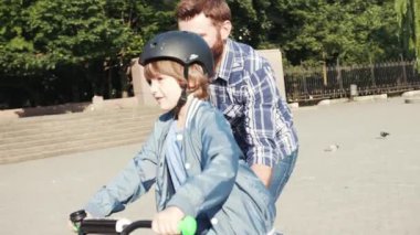 Çekici beyaz adam ve oğlu birlikte vakit geçiriyorlar. Küçük çocuk yeşil bisiklete binmeyi öğreniyor, babası bisikleti tutuyor. Mutlu çocukluk.