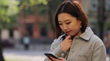 Genç Asyalı kadın akıllı telefon kullanıyor sokak kızı internet teknolojisi alışverişi yapıyor. Çin malı mobil cep telefonu işi mesajı. Yavaş çekim gönderiliyor.