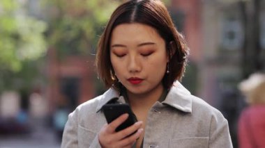 Gülümseyen Asyalı genç bir kadın sokakta akıllı telefon kullanıyor internetten alışveriş yapıyor Çin malı mobil Çin malı cep telefonu şirketinden mesaj yolluyor.