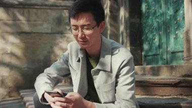 Gözlüklü mutlu Asyalı adam kameraya bakıyor. Şehir merkezinde gülümsüyor. Gün ışığında gülümsüyor.