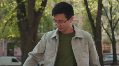 Gülümse, gözlüklü Asyalı genç adam. Telefonla mutlu sokak şehir merkezinde güneş batımını kullan. Modern, çekici, yakışıklı, başarılı, cep telefonu Japon portresi.