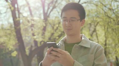 Gözlüklü genç Asyalı telefonda mutlu sokak şehir merkezinde gün batımında modern, çekici, yakışıklı, başarılı, cep telefonlu, ağır çekimli Japon portresi.