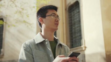 Gözlüklü Asyalı adam mutlu sokak şehir merkezini kullan günbatımı günbatımı gündelik, çekici, yakışıklı, başarılı, cep telefonu Japon yavaş çekim portresi.