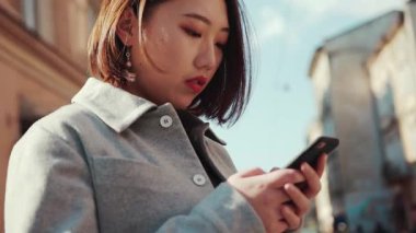 Ciddi genç Asyalı kadın, sokak güneşinde telefon kulübesi kullanıyor. Açık hava kızı internet teknolojisi alıyor. Çinli mobil Asya 'lı kadın.
