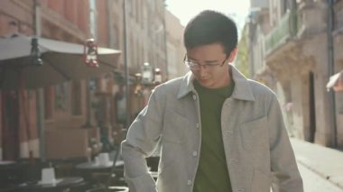 Gülümse, gözlüklü Asyalı genç adam. Telefonda konuş. Mutlu sokak şehir merkezinde, gün batımında.