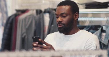 Yakından bakınca yakışıklı Afro-Amerikalı genç adam telefonuyla mesaj çekiyor. İnternetteki mutlu siyah telefon portresi. Yavaş çekim portresi tutuyor.