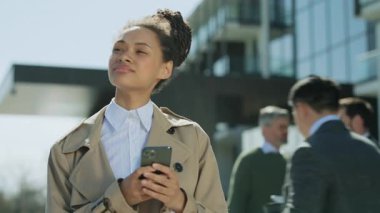 İş stili giyinmiş güzel, Afro-Amerikalı bir kadın. Telefonla yürüyor, gülümsüyor. Etrafına bak. - İnsanlar. Yavaş çekim