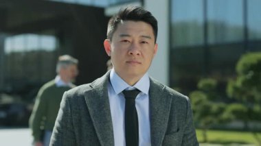 Ciddi, kendine güvenen, başarılı Asyalı iş adamı, modern ofis binasının yakınındaki resmi takım elbiseli kameraya bakıyor. Yavaş çekim