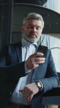 Takım elbiseli orta yaşlı bir adamın akıllı telefon ekranına bakıp modern iş merkezinin salonunda iş ortağı beklemesi. İş yerinde başarılı bir iş adamının portresi. Kapalı