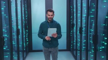 Bir bilişim teknisyeni, çok sayıda sunucuyla dolu yüksek teknolojili bir veri merkezinde özenle bir tabletle çalışır.