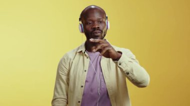 Videoda kulaklıkla neşeli bir şekilde müzik eşliğinde dans eden bir adam canlı sarı bir arkaplan karşısında kaygısız ruhunu sergiliyor.