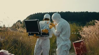 Beyaz koruyucu giysiler giymiş bir grup bilim adamı, doğada bulunan çevresel örnekleri özenle inceliyor.