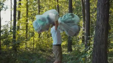 Ormandaki bir adam etrafı kirletmeyi ve korumayı ön plana çıkarır. Plastik torbalarda çöp topluyor, doğayı temizlemeye olan bağlılığını gösteriyor.