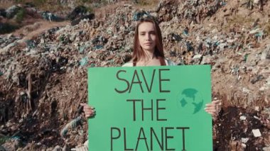 Bir eylemci, kirlenmiş enkaz ve atıklar arasında herkesi gezegeni kurtarmaya çağıran bir tabela tutuyor.