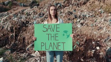 Kirli bir zemin arasında dünyayı kurtarmayı ve korumayı savunan bir tabela tutan genç bir kadın.