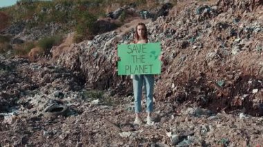 Çöpe atılmış bir arazide elinde gezegenin korunmasını savunan bir levha tutan genç bir aktivist var.