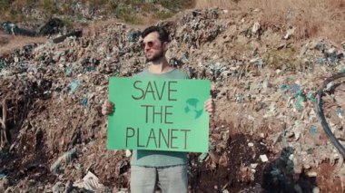 Bir aktivist, plastik atık yığınları arasında bir Gezegeni Kurtarın tabelası tutuyor ve acil çevre sorunlarını vurguluyor