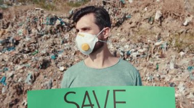 Kendini adamış bir eylemci, çevresel değişime duyulan acil ihtiyacı vurgulayarak, bir çöp sahasının önünde dimdik duruyor.
