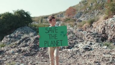 Genç bir çocuk ıssız bir bölgede tabela tutarken çevrenin korunmasını tutkuyla savunuyor.