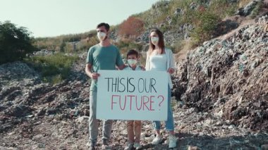 Kirli bir ortamda gelecekleri hakkındaki endişelerini ifade eden bir tabela tutan bir aile bir arada duruyor.