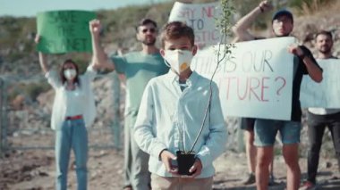 Genç bir çocuk, bir protesto sırasında acil iklim müdahalesini savunan yeşil bir bitki tutuyor.