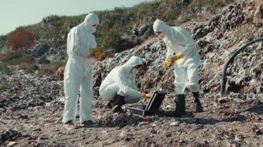 Koruyucu giysiler giymiş bir grup araştırmacı, kirlenmiş bir bölgeden toplanan toprak örneklerini dikkatle analiz ediyor.