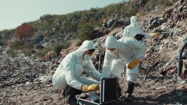 Koruyucu giysili iki kişi tehlikeli bir bölgede kapsamlı bir soruşturma yürütüyor.