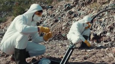 Koruyucu giysiler giyen iki bilim adamı detaylı analiz için kirlenmiş toprak örneklerini dikkatle inceliyor.