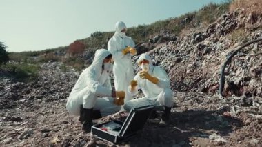 Tehlikeli madde giysisi giymiş bir grup araştırmacı uzak bir yerde toprak kirliliğini araştırıyor.