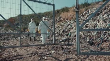 Koruyucu giysiler içindeki bilim adamları çeşitli enkazlarla çevrili tehlikeli bir atık alanını dikkatle inceliyorlar.