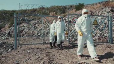 Koruyucu giysiler giymiş bir grup bilim adamı uyarı işaretleriyle işaretlenmiş güvenli bir alanda dikkatle geziniyor.