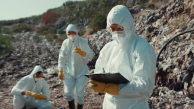 Tehlikeli madde giysileri içindeki araştırmacılar, kritik çevre çalışmaları için kayalık arazideki toprak örneklerini titizlikle analiz ediyorlar.