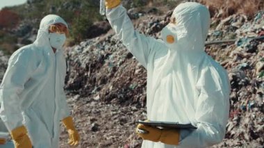 Koruyucu giysiler giymiş iki araştırmacı tehlikeli bir ortamda çeşitli örnekleri titizlikle inceliyor.