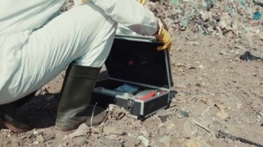 Kendini adamış bir araştırmacı tehlikeli, atık ve kirlenmiş bir bölgede çeşitli araçları dikkatle inceler.