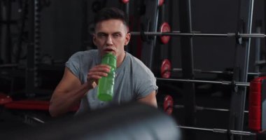 Ciddi bir adam spor salonunda dinlenirken su içerken kameraya bak akıllı saat şişesi yüz vücut çalıştırma sporu genç erkek vücut geliştirme yakışıklı portresi.