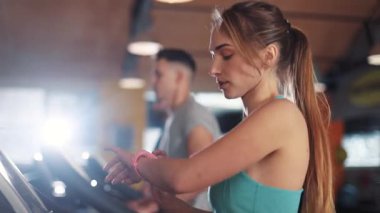 Koşu bandındaki güzel genç kadın spor salonu ışık spor spor spor fitness internet yüz teknolojisi spor spor spor spor kıyafetleri vücut egzersizi ağır çekimde akıllı telefon kullanıyor.