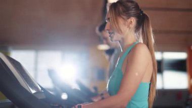 Koşu bandındaki çekici genç kadın spor spor spor spor fitness internet yüz teknolojisi spor spor spor kıyafetleri vücut egzersizi ağır çekimde akıllı telefon kullanıyor.