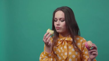 Turuncu bluzlu komik bir kadının makaronu yediği, diğer elinde iki tane daha tuttuğu, kurabiyeyi ısırdığı, doğrudan kameraya baktığı, gözlerini vidaladığı ve kafasını salladığı yakın görüntü. Yavaş çekim