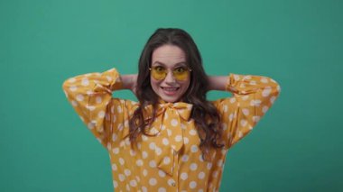 Güneş gözlüklü güzel kıvırcık kadın saçlarını okşuyor ve kameraya gülümsüyor. Pozitif ruh hali, iyi hissetmek, gerçek duygular. Yakından bak, kadın portresi