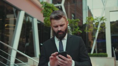 NEW YORK - 5 Nisan 2017: Başarılı bir iş adamı, büyük şehir ticaret bölgesi ofisinin üzerinde yürürken akıllı telefon kullanır.