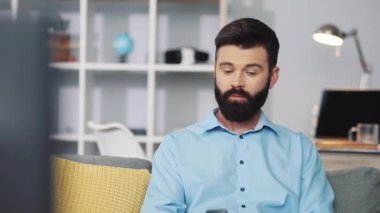 Rahat ve rahat bir oturma odasında televizyon izlerken uzaktan kumanda kullanmaya odaklanmış bir adam.