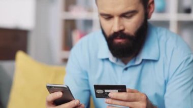Bir adam evde rahat bir şekilde kredi kartı ve akıllı telefonunu kullanarak online alışverişi başarıyla tamamlar.