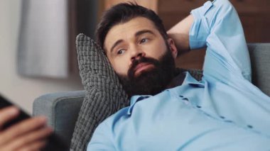 Bir adam rahat bir şekilde kanepede uzanıyor, dikkatle ekranına bakıyor, boş zamanlarının tadını çıkarıyor.